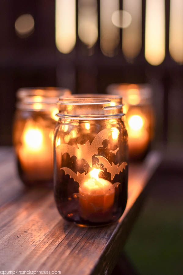 mason jar with etched glass look flying bats on it, and lighted candle inside, other ones blurry in the background