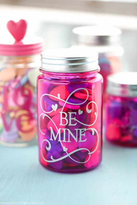 pink mason jar with sparkly vinyl letters reading be mine on it and conversation hearts filling it