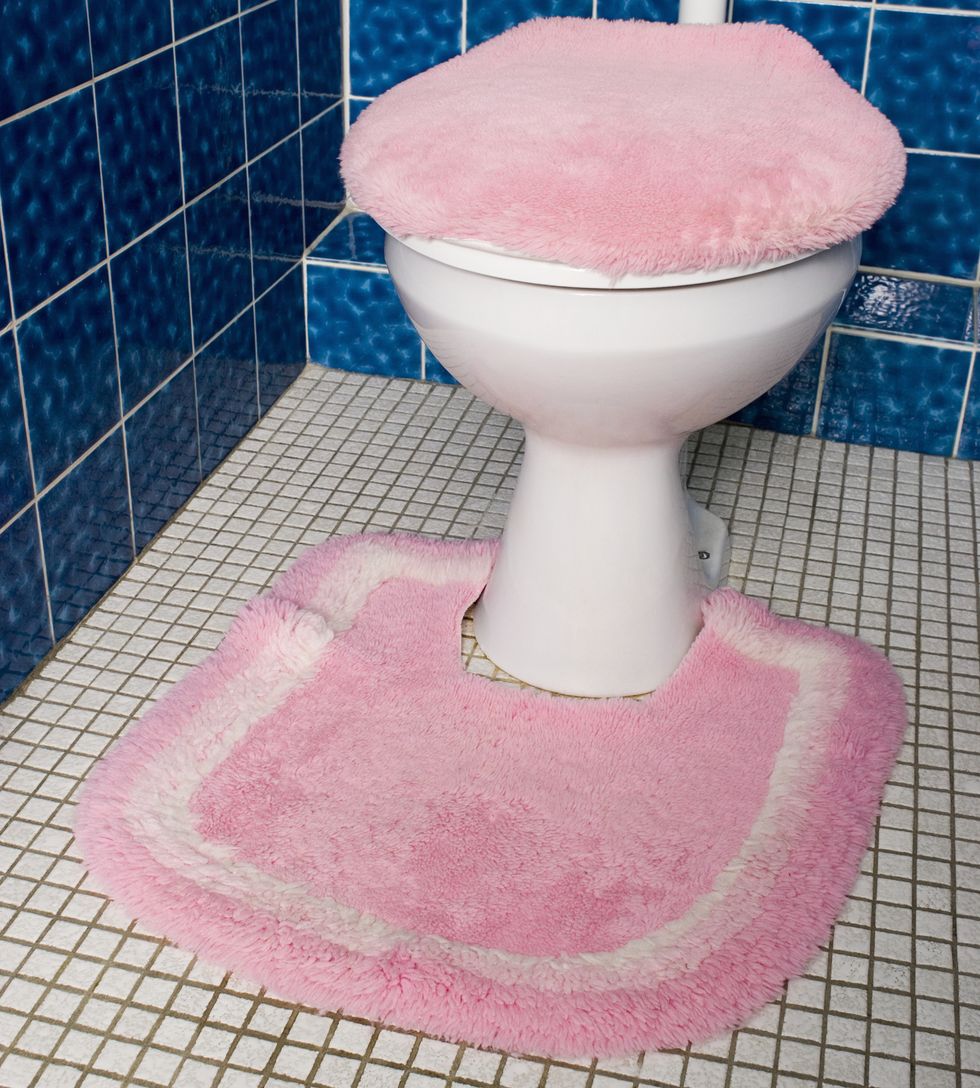 A toilet with fluffy pink seat cover and rug