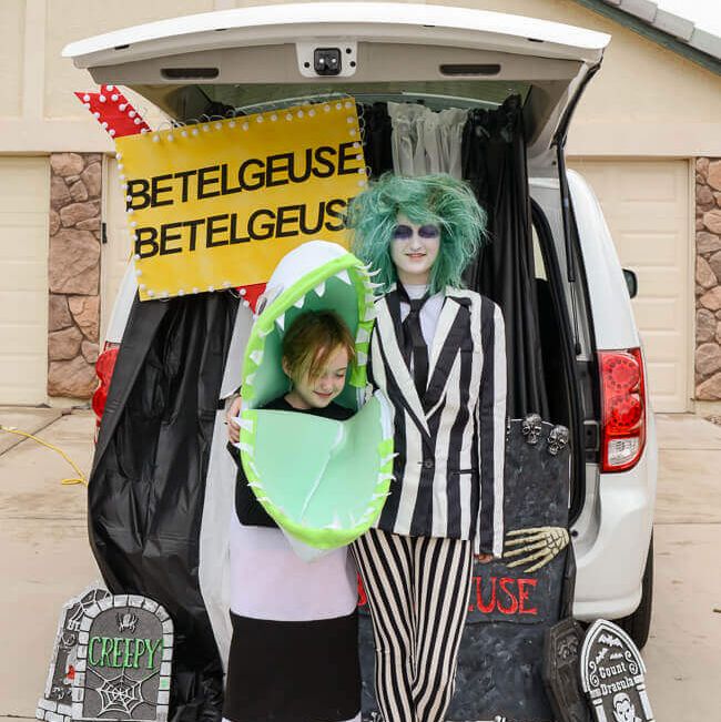 a car decked out for trunk or treat in a beetlejuice with a light up sign and people dressed like beetlejuice and a sand worm in front