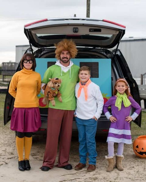 a car decked out for trunk or treat in a scooby doo them with a mystery machine backdrop and a family dressed as the show's characters in front