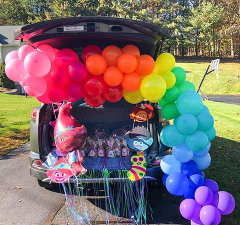 a car decked out for trunk or treat in a trolls theme with a rainbow balloon arch and trolls characters