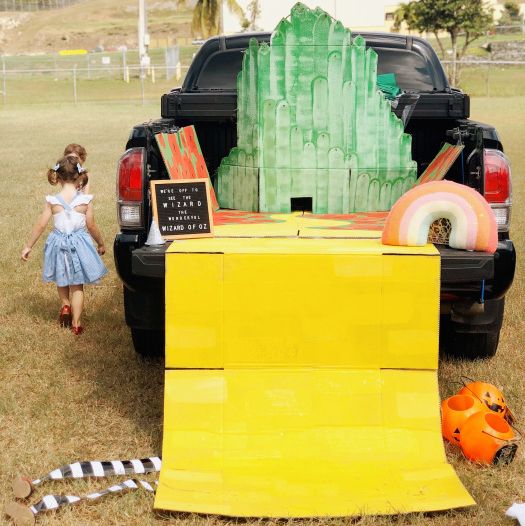 a car decked out for trunk or treat in a wizard of oz theme with an emerald city, a yellow brick road and striped witch legs sticking out of the bottom