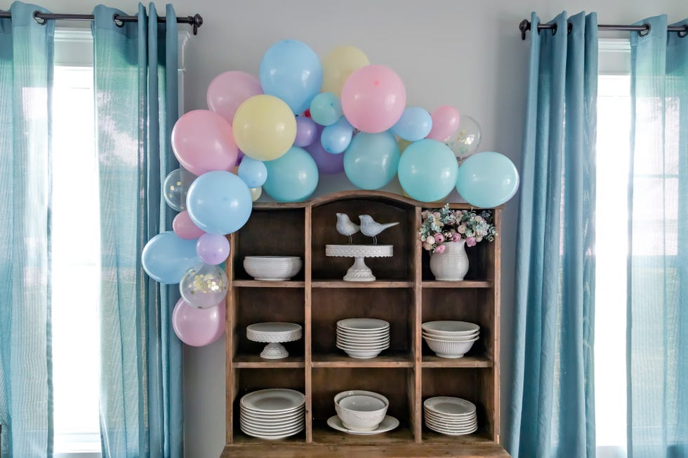 a vintage rustic wood china hutch decorated with a balloon arch in pastel colors for a baby shower or birthday party