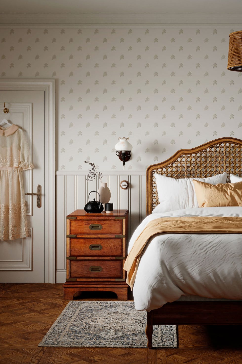 a cosy white bedroom featuring a bed with a white duvet, a wooden bed nightstand, and a dress hanging on the door