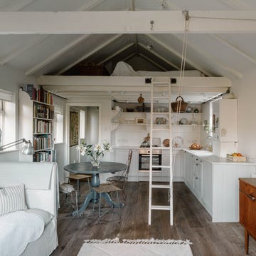 A white London studio apartment a white studio apartment with exposed rafters, a ladder, an integrated kitchen, and a dining table