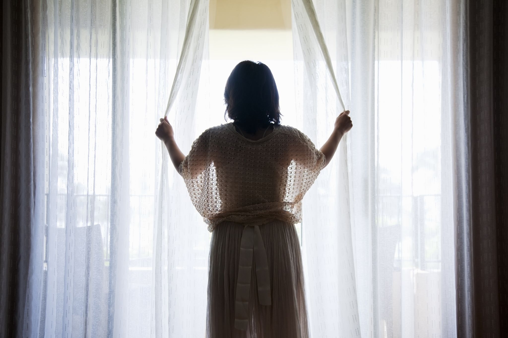 woman opening curtains of hotel room