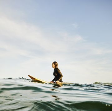 wide shot of female surfer sitting on surfboard in ocean while waiting for wave during sunrise surf session