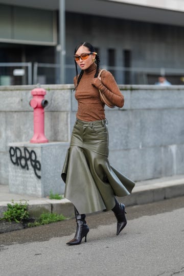 milan, italy september 19 a guest wears dark brown sunglasses, gold earrings, dark brown long sleeve sheer mesh shirts, dark brown leather bag, shiny dark green leather midi skirt, shiny black pointed toe heeled leather boots, outside philosophy, during the milan fashion week springsummer 2024 2025 on september 19, 2024 in milan, italy photo by edward berthelotgetty images