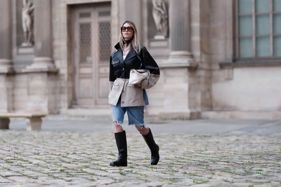 paris, france march 30 natalia verza wears blue ripped denim shorts, a bi color black and beige leather jacket short trench coat from munthe, square toe knee high black leather boots by agl, a cream leather bag by tods, a little scarf by chanel, sunglasses by celine, during a street style fashion photo session, on march 30, 2024 in paris, france photo by edward berthelotgetty images