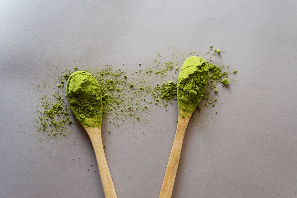 a wooden spoon with green matcha powder on a gray background in the morning sunlight