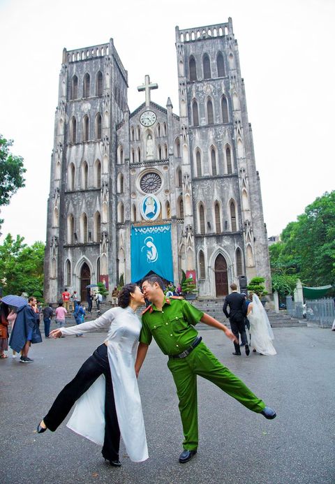 In het hart van de Oude Wijk voor de beroemde SintJozefkathedraal poseren een politieagent en zijn bruid voor een huwelijksfotograaf Deze speelse houding duidt op een nieuw moderner Vietnam