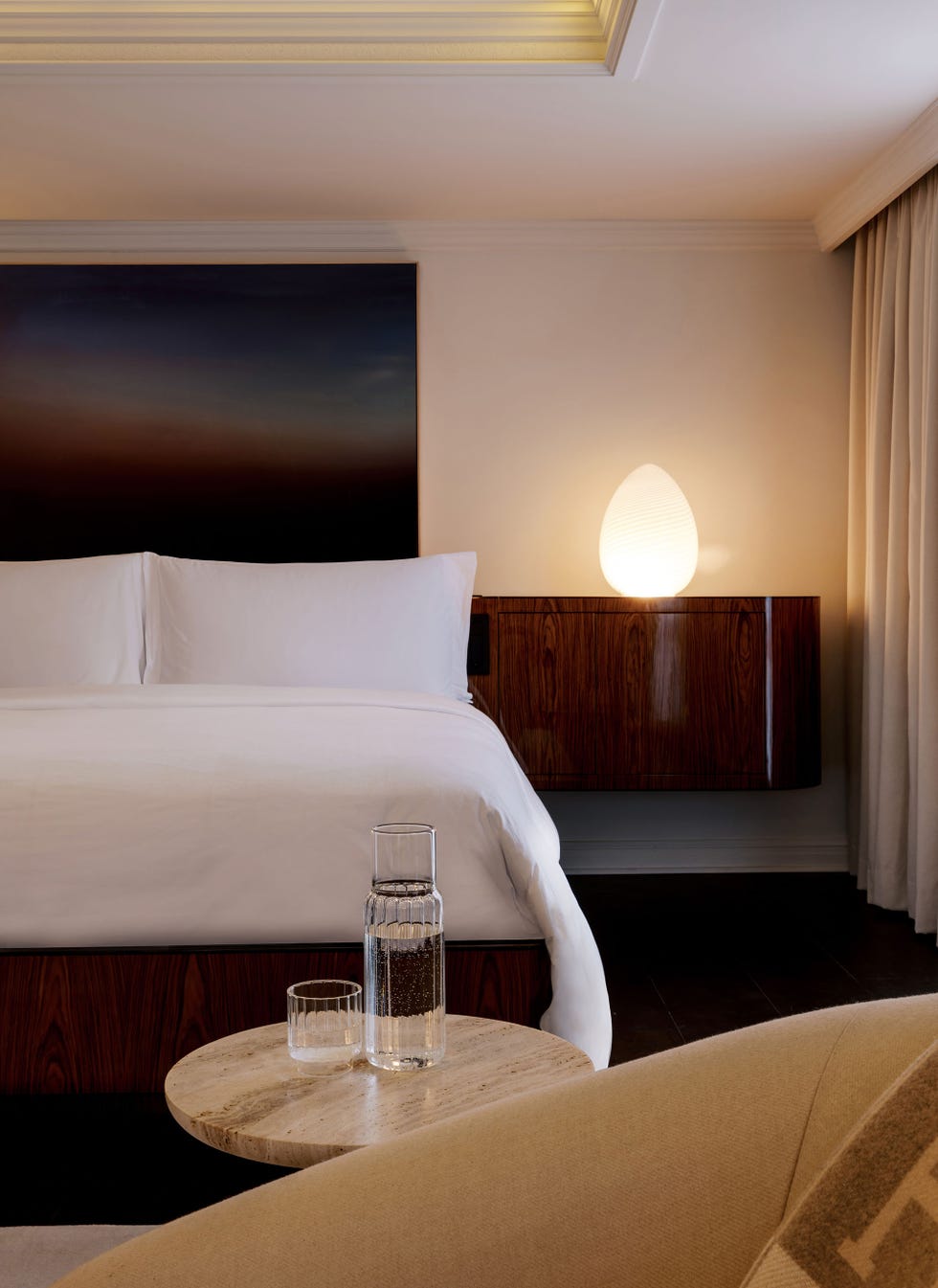Modern bedroom showcasing a bed, a side table with a glass, a water carafe, and a lamp.