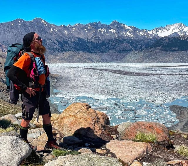 hiker standing on rocky terrain overlooking a glacier and mountain range
