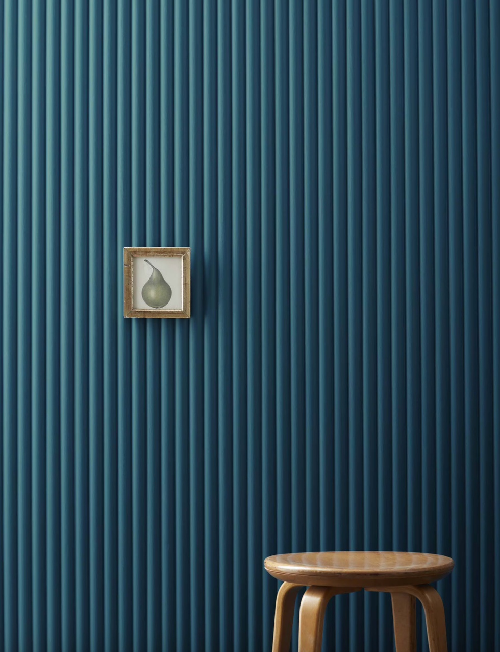 Textured blue wall with a framed artwork and a wooden stool.