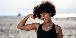 fit young woman on the beach flexing her biceps woman with curly hair wearing sports clothing looking at camera