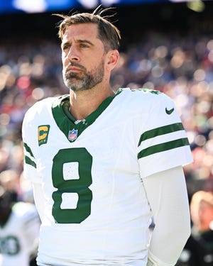 aaron rodgers stands and looks to the left, he wears a white football jersey for the new york jets