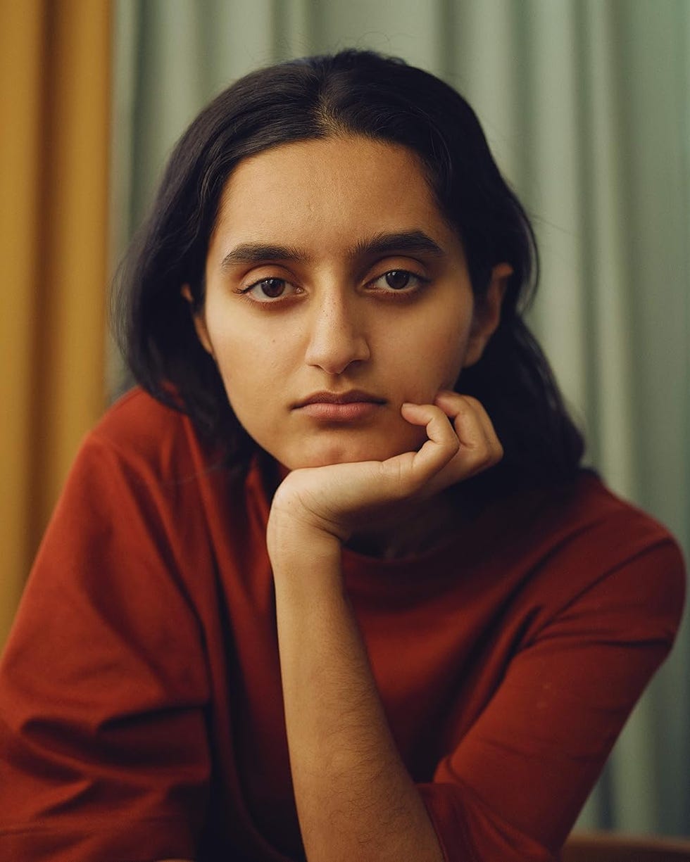 a woman resting her chin on her hand wearing a red top
