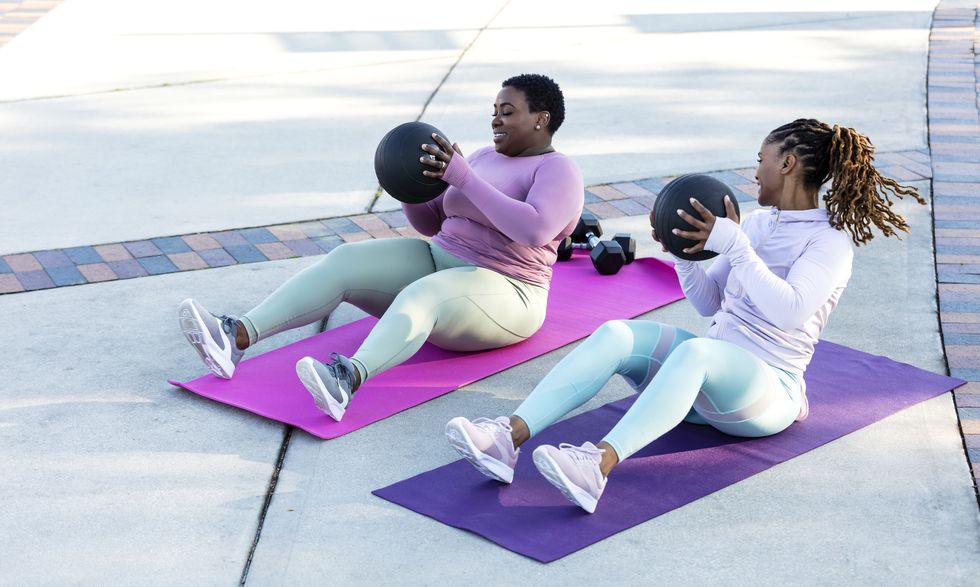 two women exercising together outdoors wearing long sleeved sports doing sit ups
