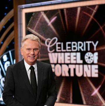 pat sajak smiling for a photo in front of the wheel of fortune logo