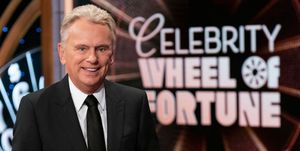 pat sajak smiling for a photo in front of the wheel of fortune logo