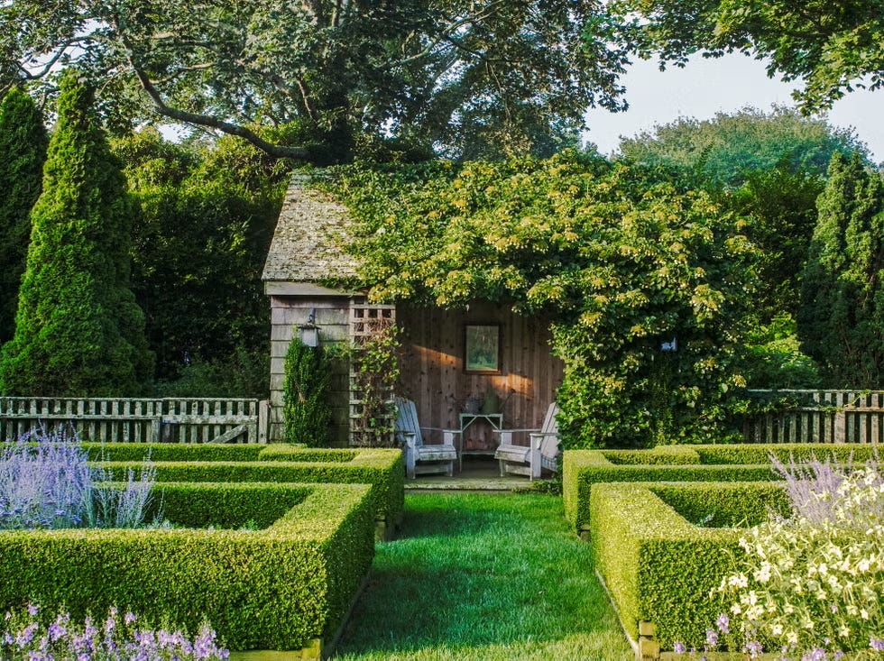 Garden scene featuring a wooden shed surrounded by neatly trimmed hedges and seating.