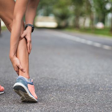 Achilles injury on running outdoors. Women holding Achilles tendon by hands close-up and suffering with pain. Ankle twist sprain accident in sport exercise running jogging.