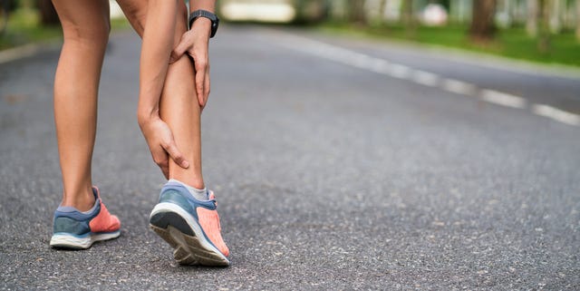 Achilles injury on running outdoors. Women holding Achilles tendon by hands close-up and suffering with pain. Ankle twist sprain accident in sport exercise running jogging.