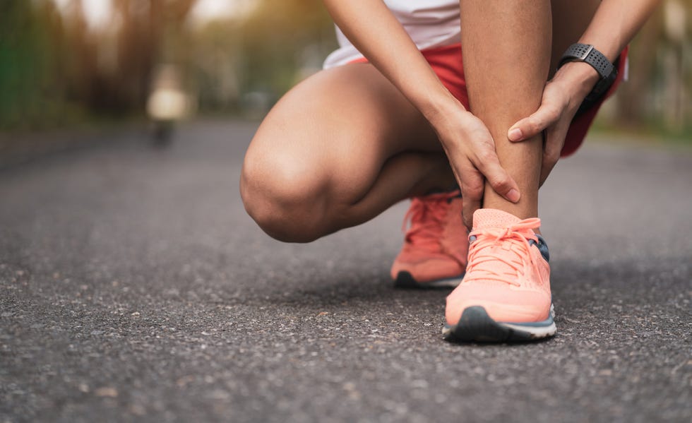 woman in athletic walking shoes holding shin in pain