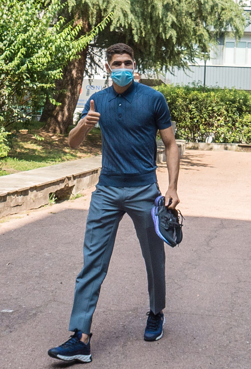 achraf hakimi, de cuerpo entero, saliendo de un reconocimiento médico en milán italia con unas zapatillas de deporte en la mano