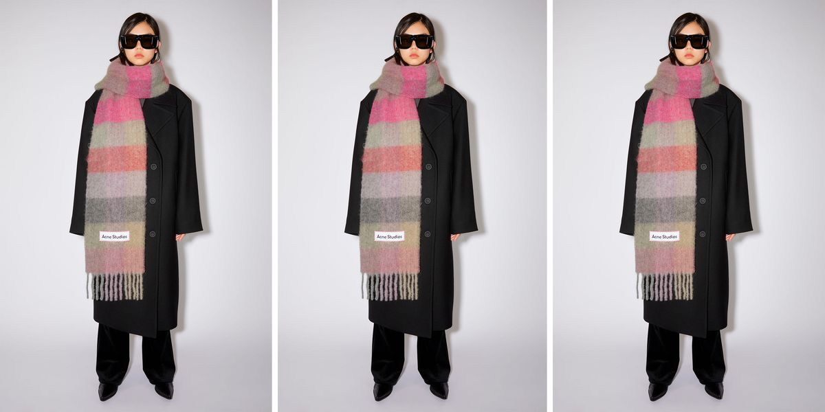 a model wears a plaid acne studios scarf over a black jacket and pants in a post about the acne studios scarf 2022