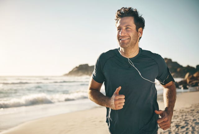 active, fit and healthy man jogging on a beach while listening to music on earphones with stunning outdoor clear sky and sea copy space happy, mature and athletic guy running, doing fitness exercise