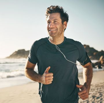 active, fit and healthy man jogging on a beach while listening to music on earphones with stunning outdoor clear sky and sea copy space happy, mature and athletic guy running, doing fitness exercise