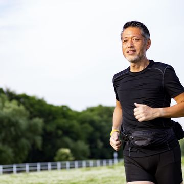 active japanese senior man jogging against the sunshine
