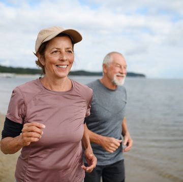 active senior couple runners jogging outdoors on sandy beach by sea in early morning.