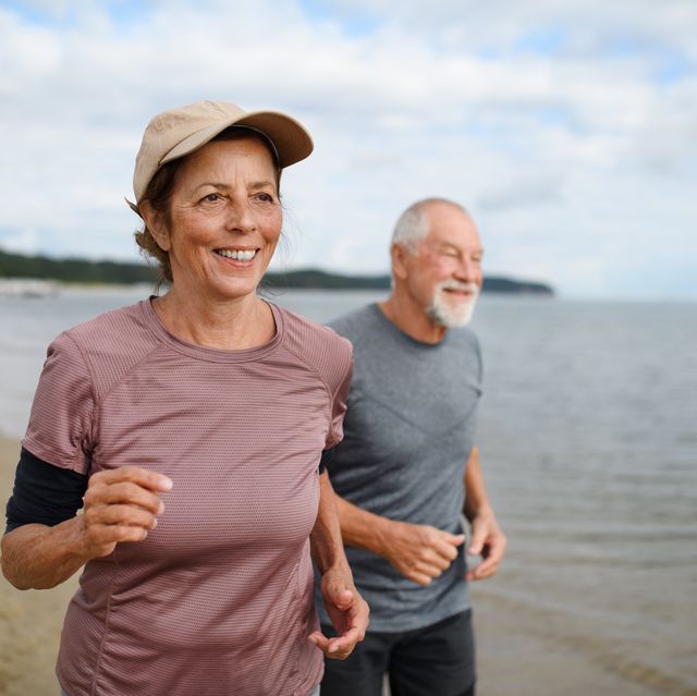 active senior couple runners jogging outdoors on sandy beach by sea in early morning.