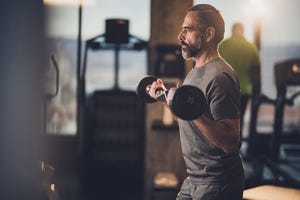 active senior man having strength exercise with barbell in a gym