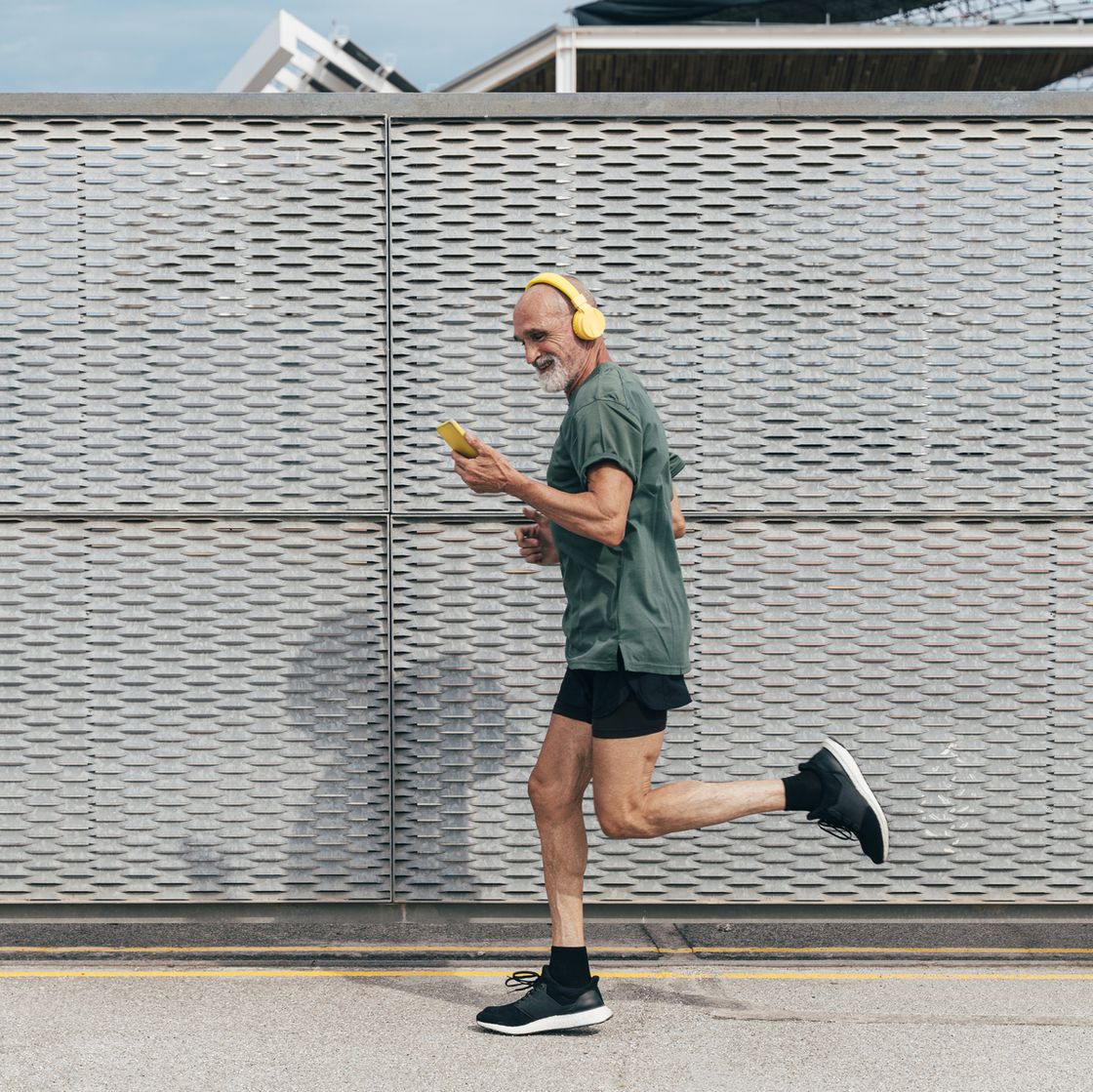 active senior man listening to music and running by fence