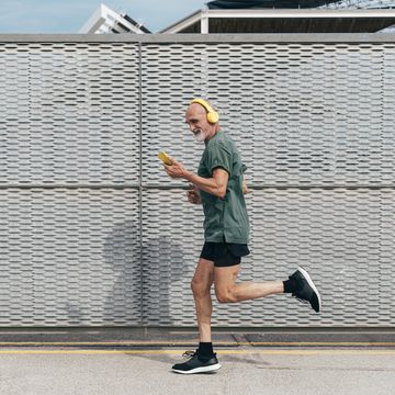 active senior man listening to music and running by fence