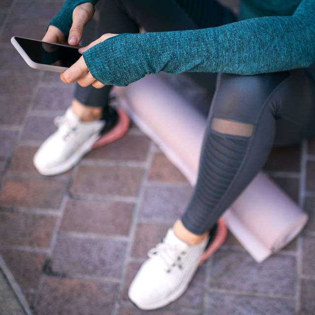 Active sports woman using her mobile phone while sitting in a city street