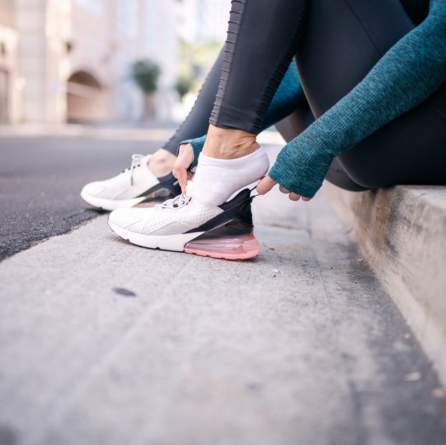 Active woman putting her sneaker on while sitting on a street sidewalk