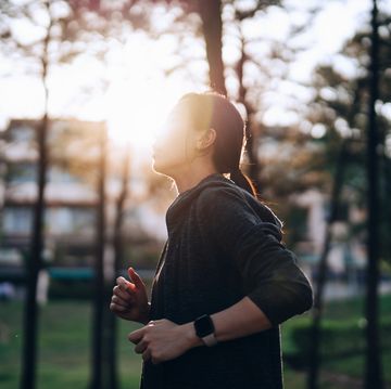 active young asian woman jogging outdoors in neighbourhood against morning sunlight, with houses and trees in background health and fitness training healthy living lifestyle wellbeing and wellness personal challenge sports and exercise concept