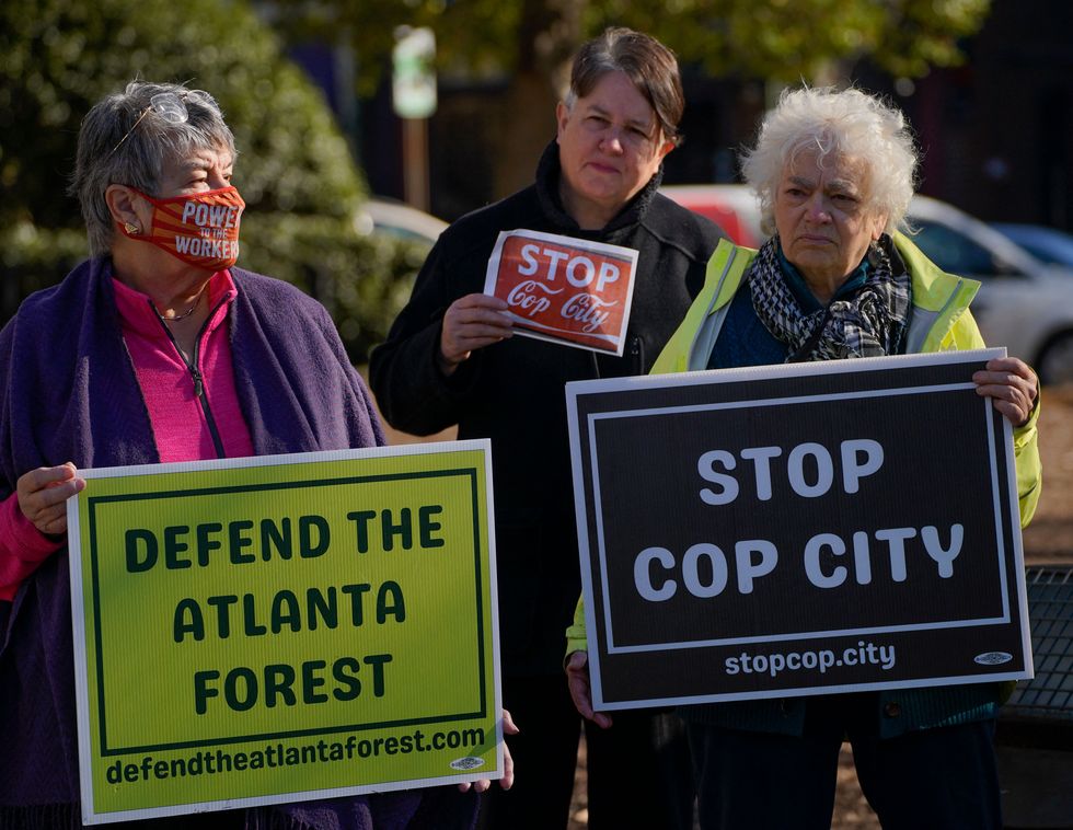 activists hold signs that read defend the atlanta forest and stop cop city