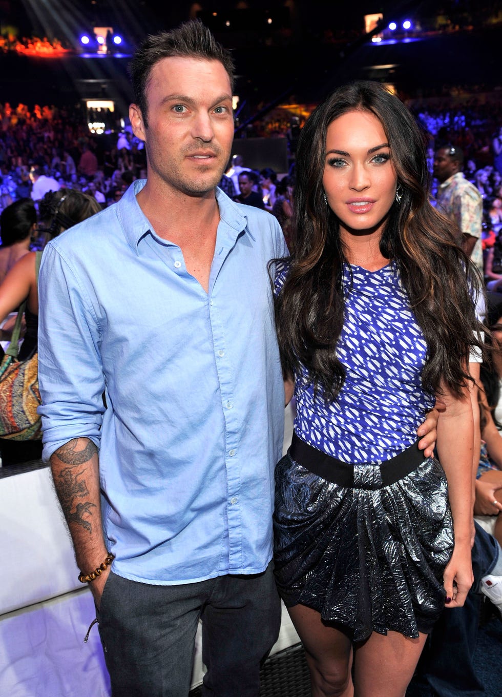 brian austin green and megan fox stand together and pose for a photo, a crowded room is behind them