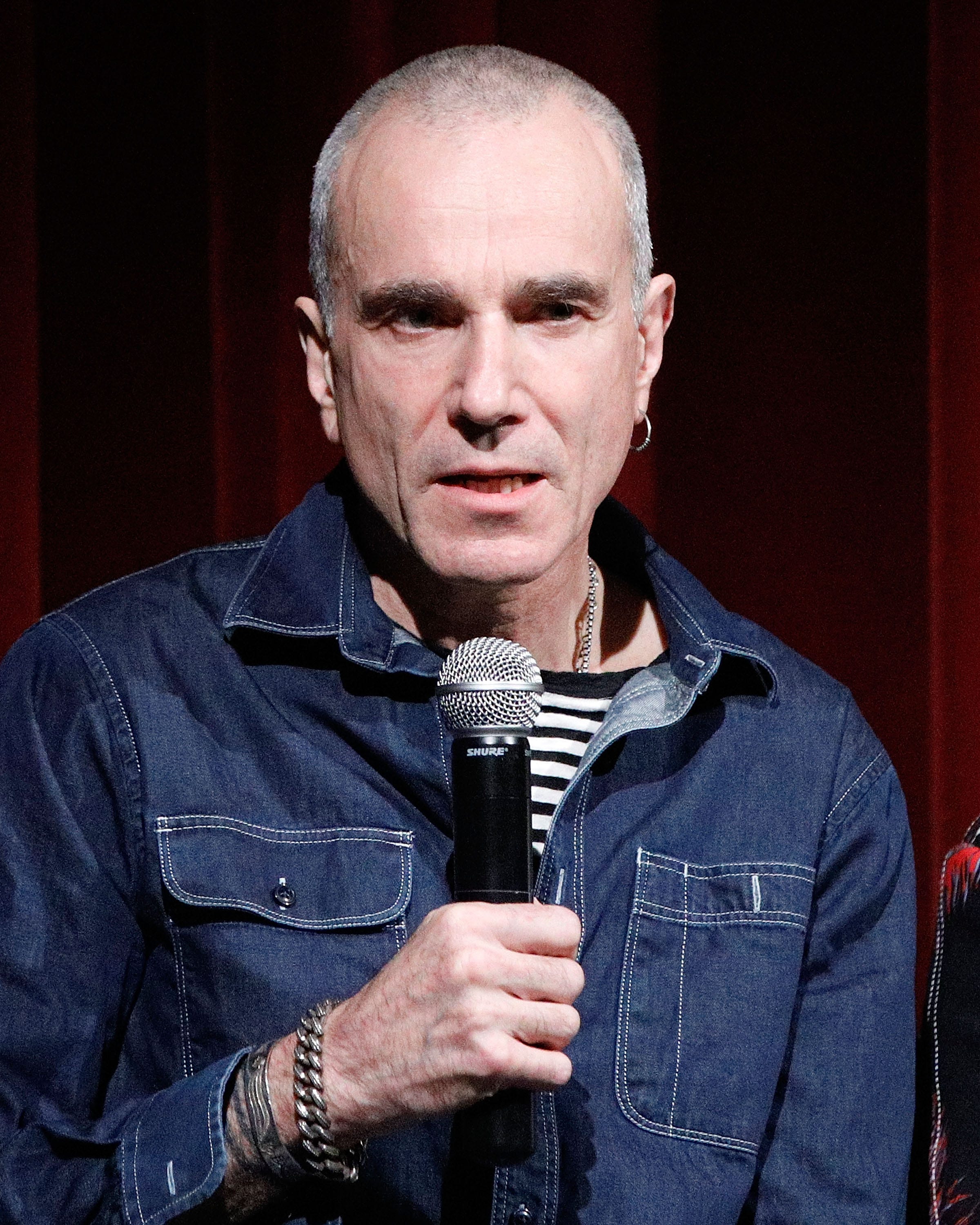 actor daniel day lewis holding a microphone with his right hand while speaking to an audience