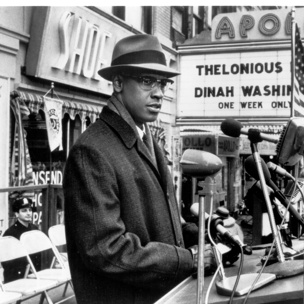 denzel washington dressed as malcolm x stands outside an apoolo theater with several microphones in front of him