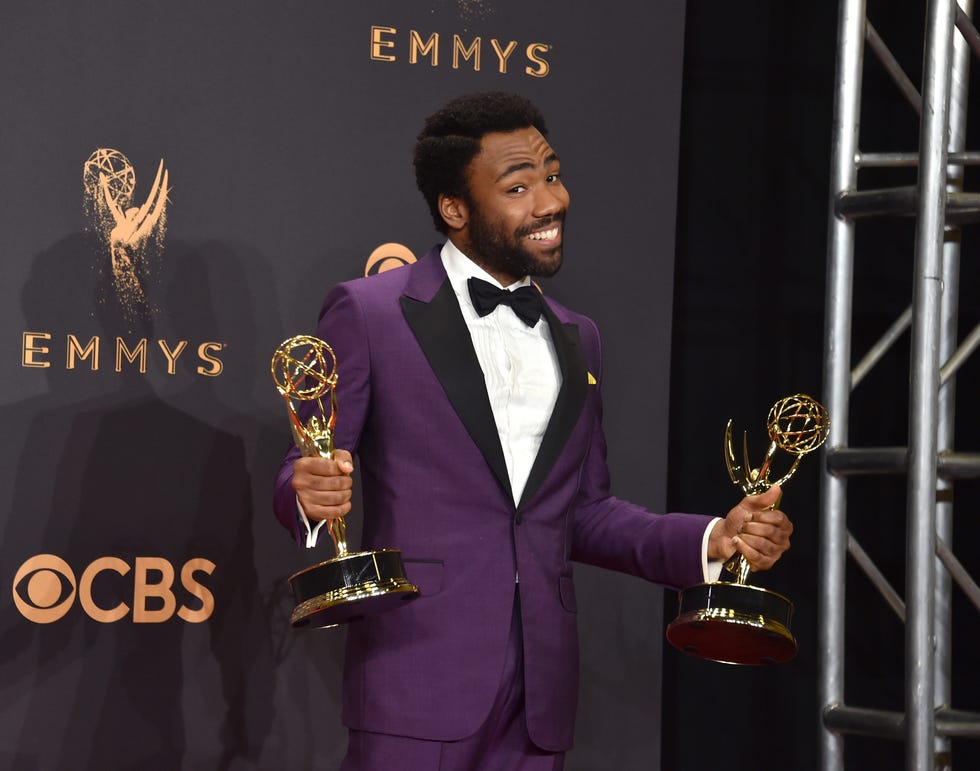 donald glover wearing a purple tuxedo and smiling while holding an emmy trophy in each hand