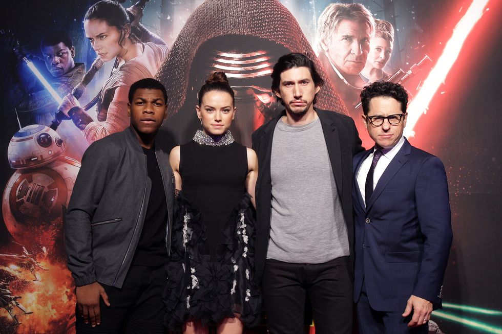 john boyega, daisy ridley, adam driver, and jj ﻿abrams pose for a photo while standing in front of a star wars movie background