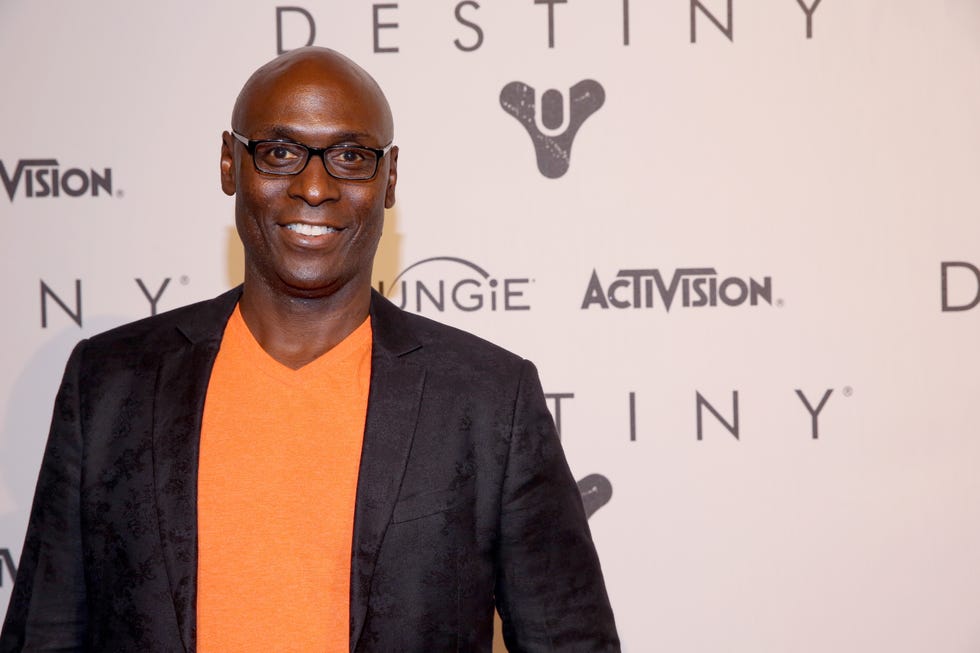 lance reddick, wearing a black suit jacket and orange shirt