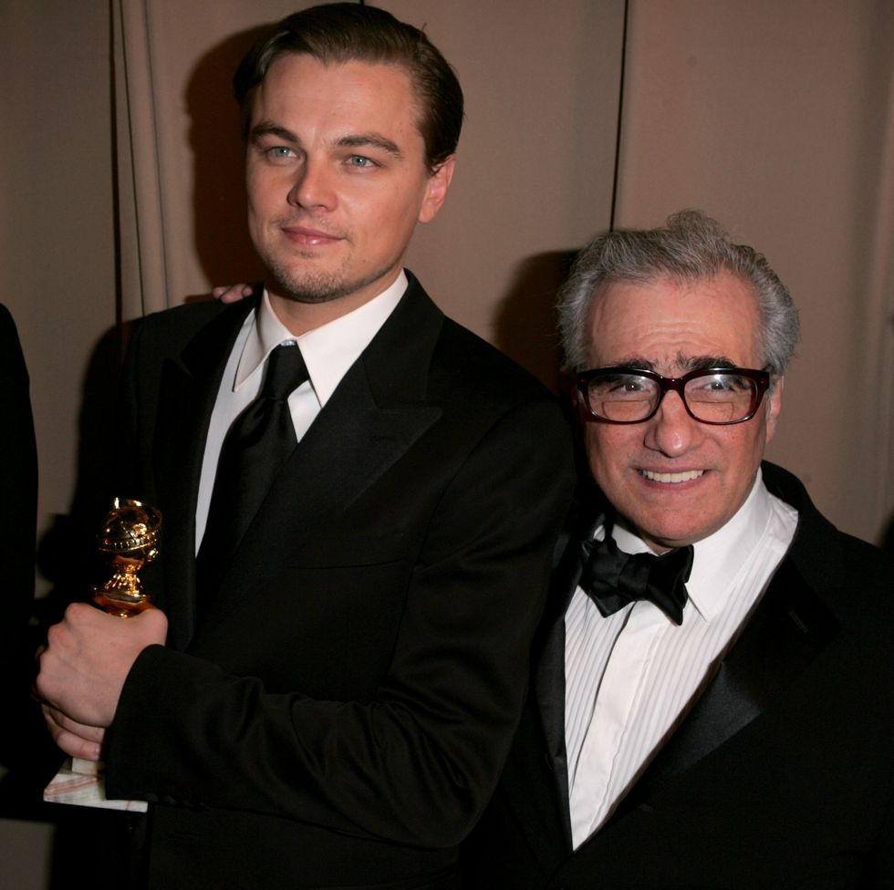 leonardo dicaprio stands next to martin scorsese who has an arm on dicaprios should, dicaprio grips a golden globe statue with both hands and looks to the left of the camera, scorsese smiles and looks to the right of the camera, dicaprio wears a black suit and tie with a white collared shirt, scorsese wears a black tuxedo with a white shirt